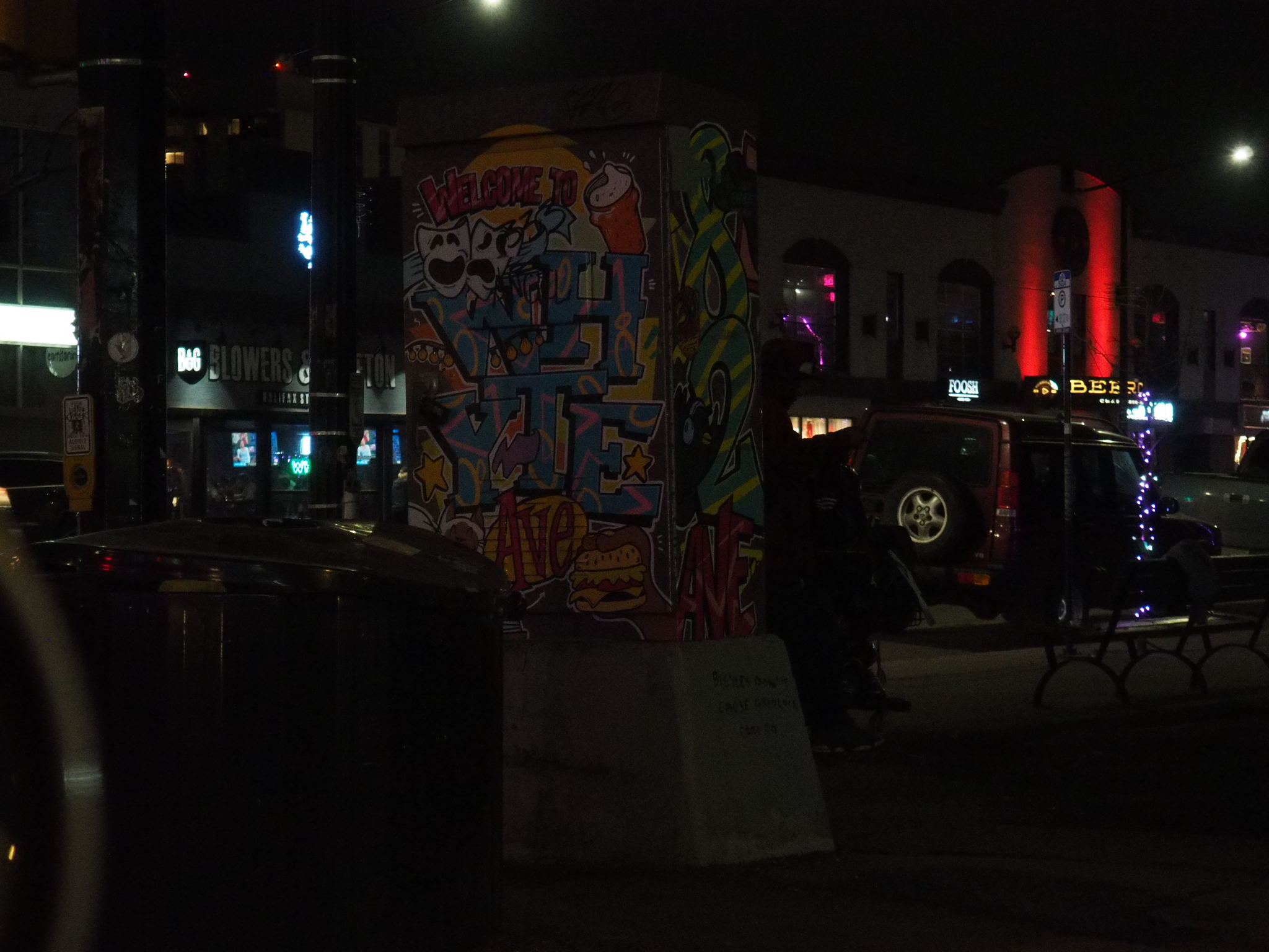 night street corner with murals, parked cars, benches, and colored lights in edmonton