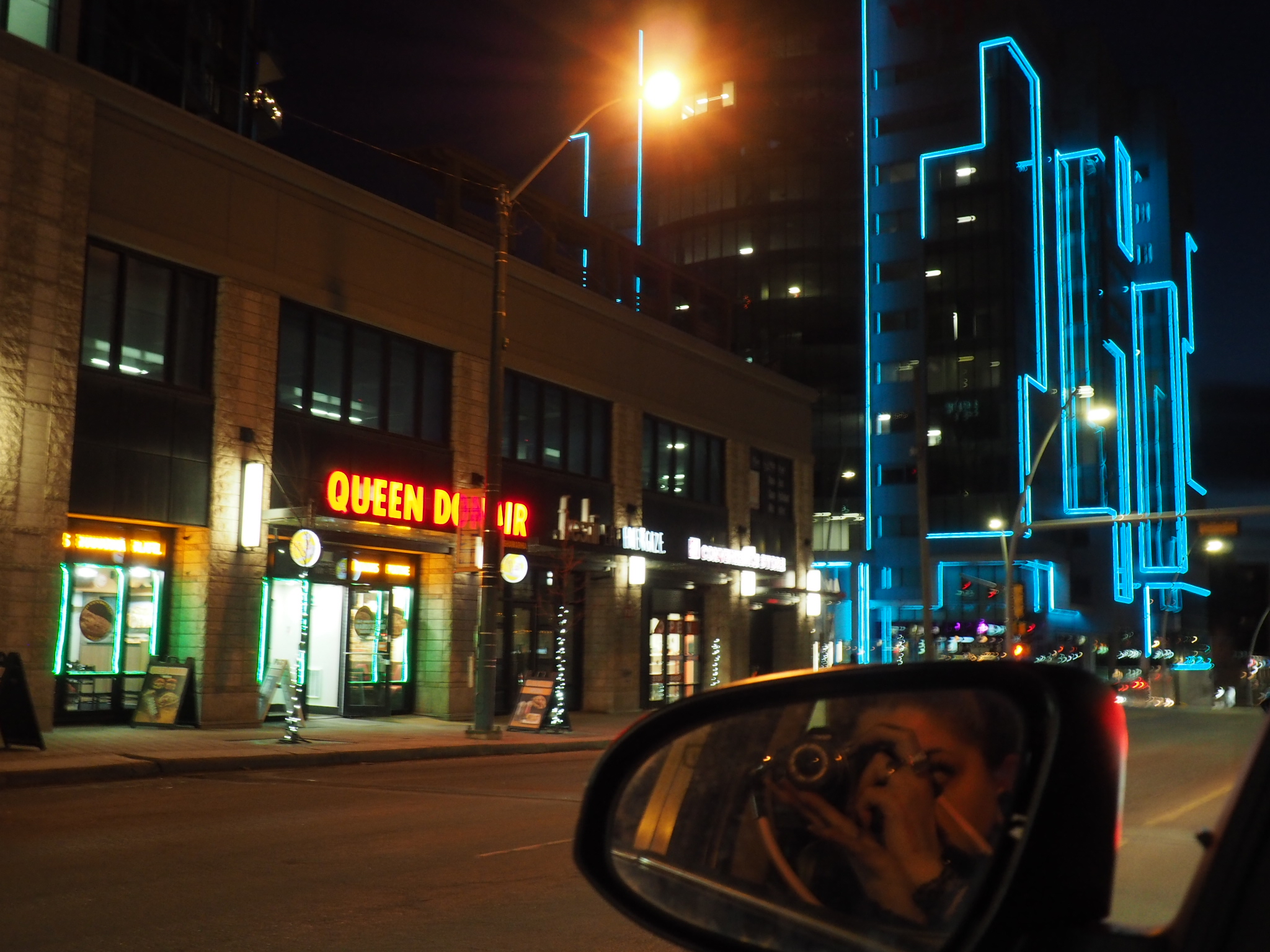 blue-lit downtown building and storefronts seen from a car in edmonton at night