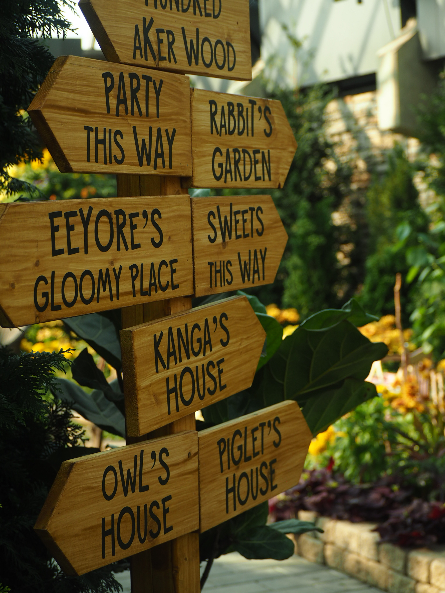 painted wooden garden signs pointing toward storybook places including eeyore's and kanga's houses