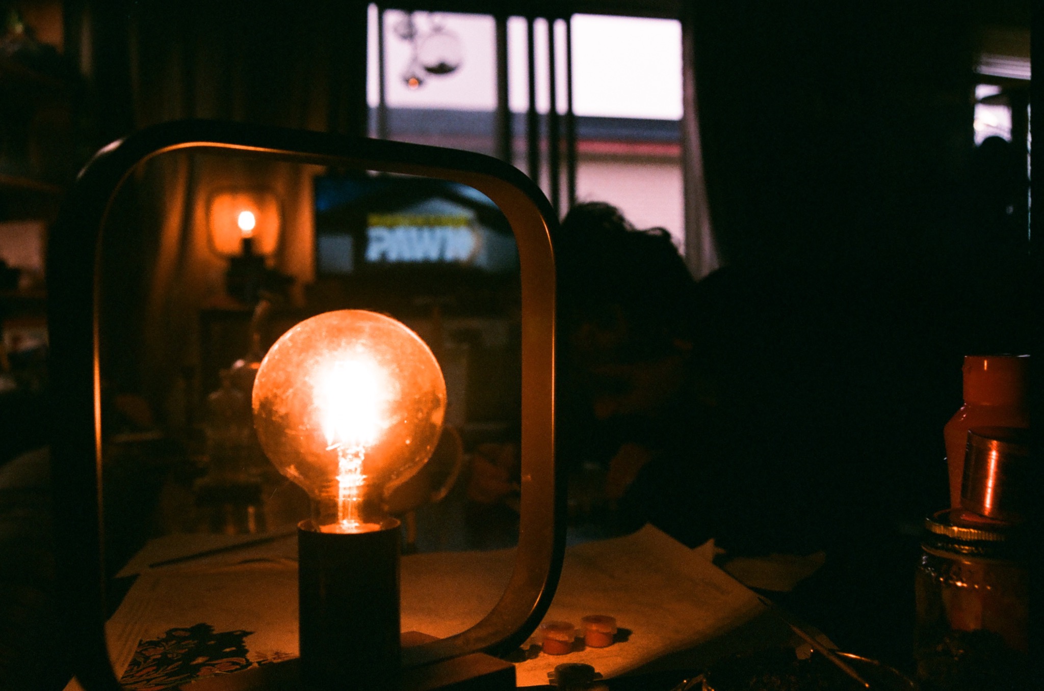 a warm glowing edison bulb sits on a dark table, illuminating papers in a dim room.
