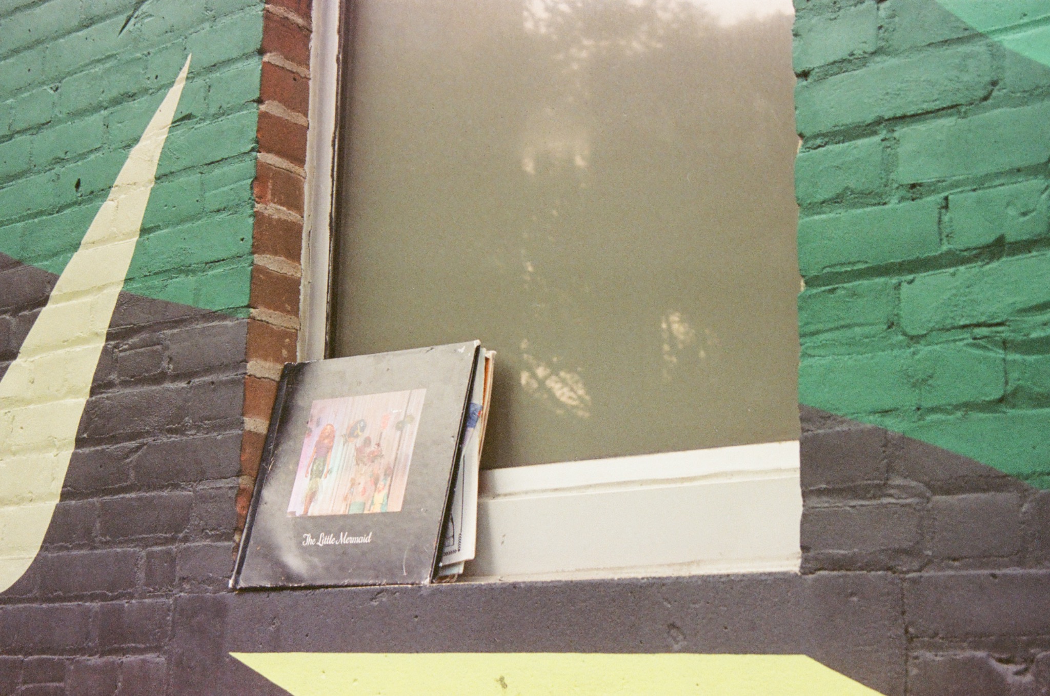 a book titled 'the little mermaid' on a window ledge next to a green and black brick wall.