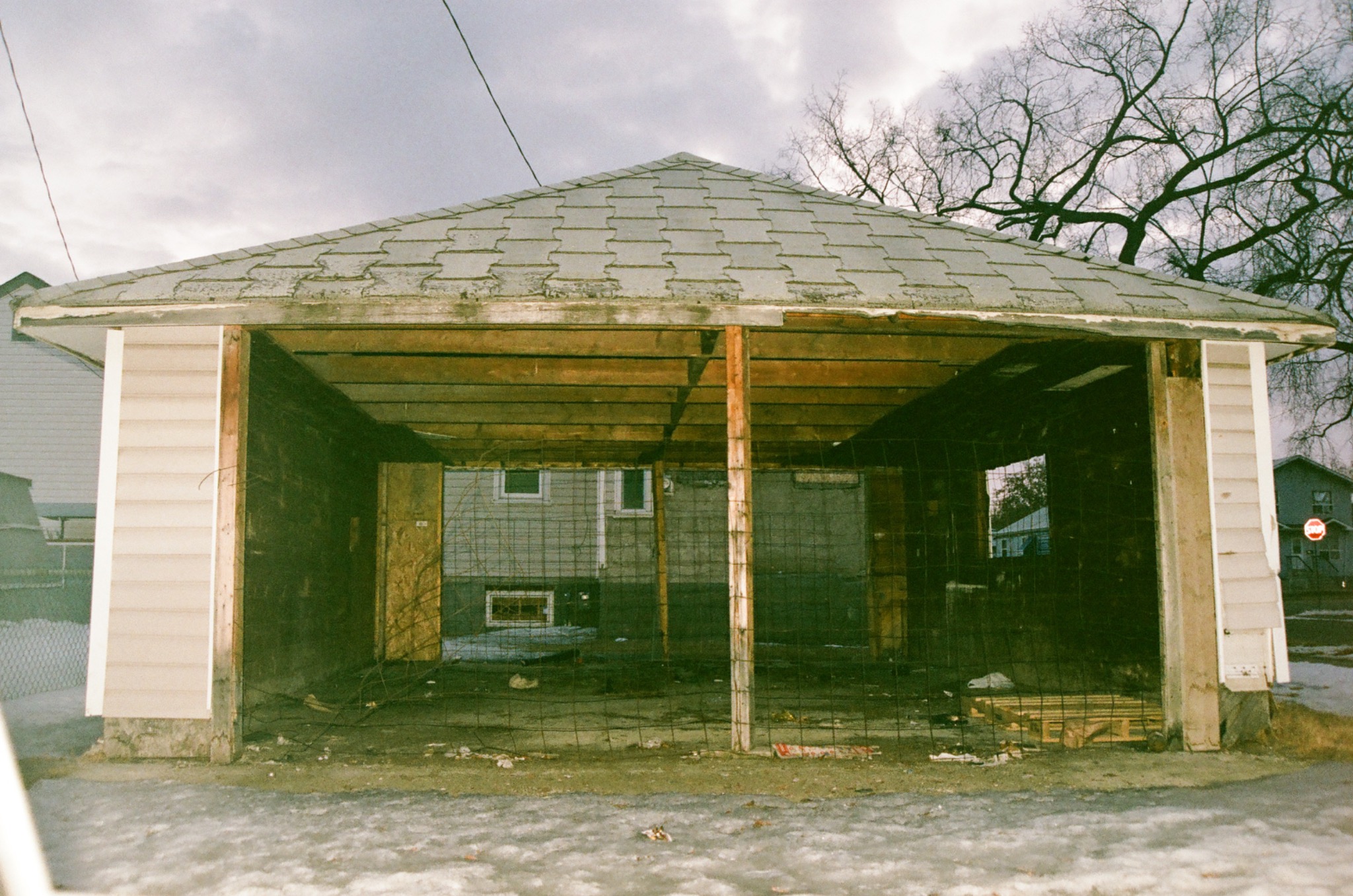 abandoned garage with exposed wooden beams and wire fence in winter, cloudy sky.