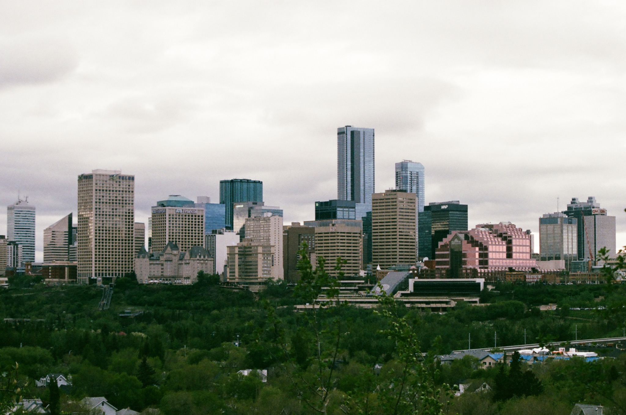 a sprawling city skyline with diverse buildings and green trees under an overcast sky.