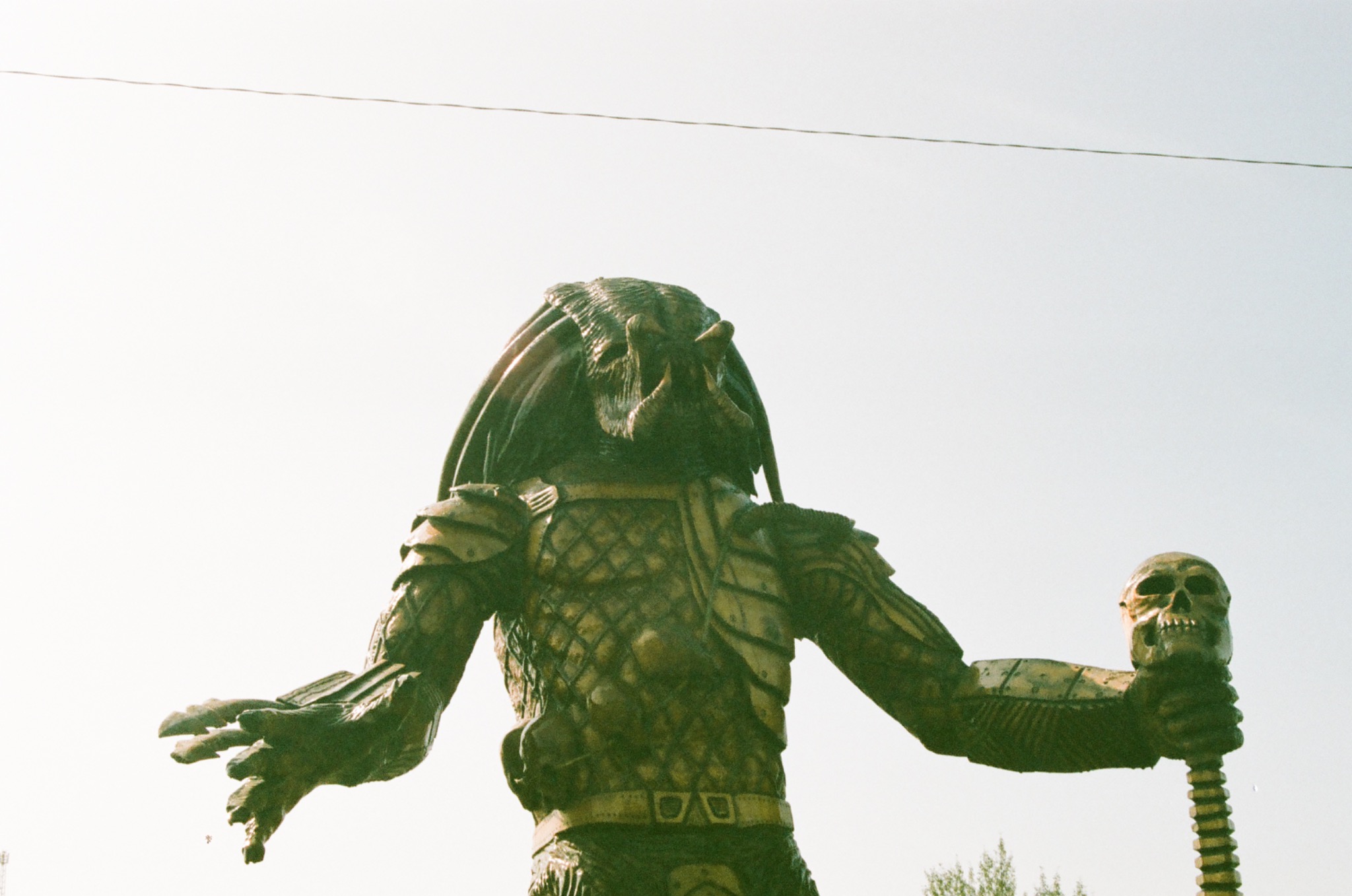 predator statue holding a staff with a human skull against a bright sky.
