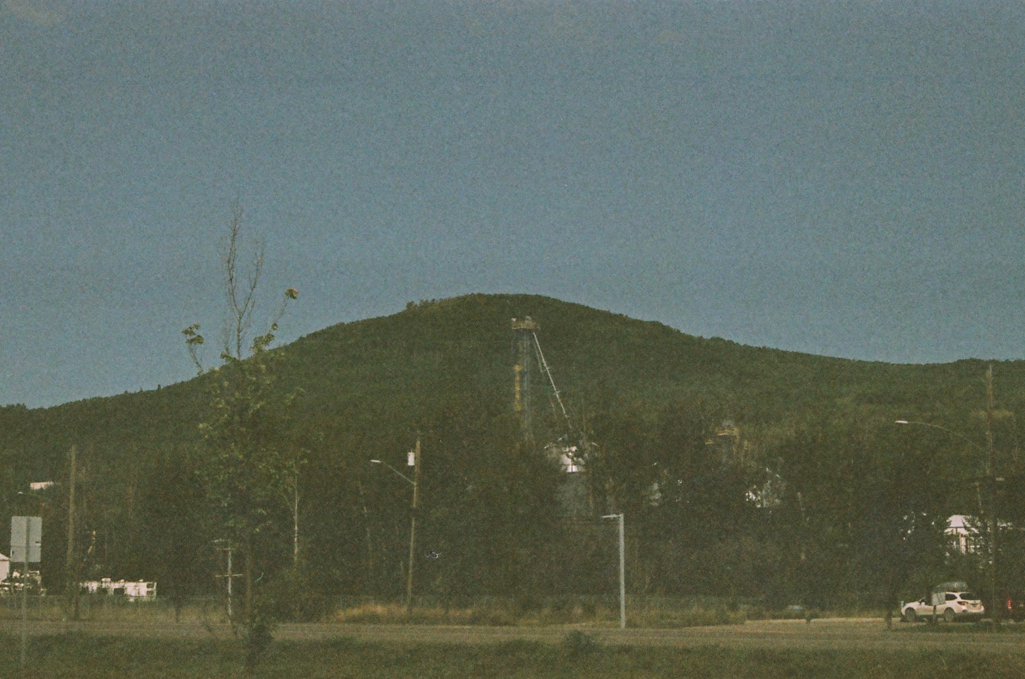 a grainy photo of a green, tree-covered hill with a tower structure and a road in the foreground.