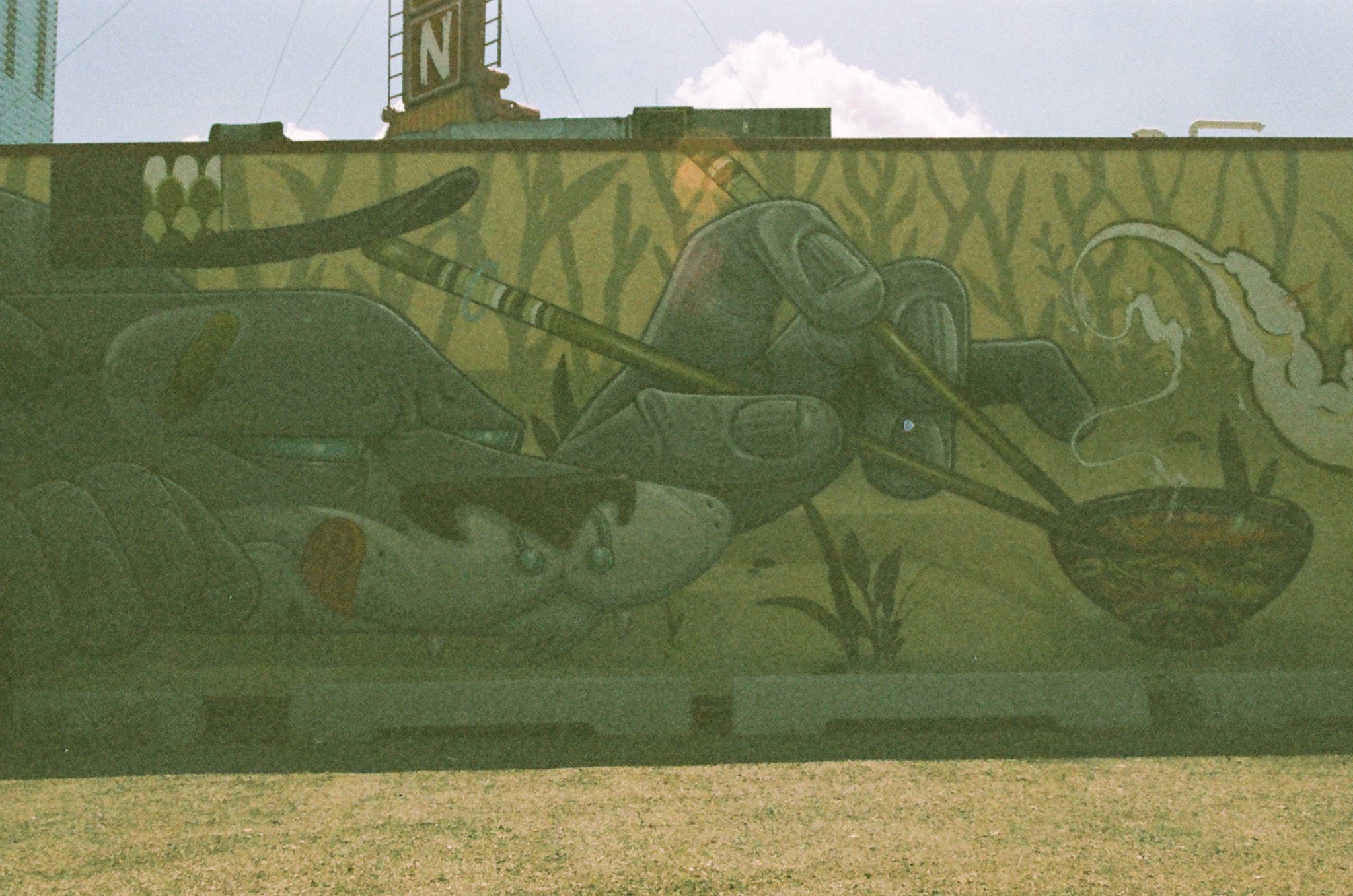 a grainy photo of a mural depicting large hands holding chopsticks over a steaming bowl on a green wall.