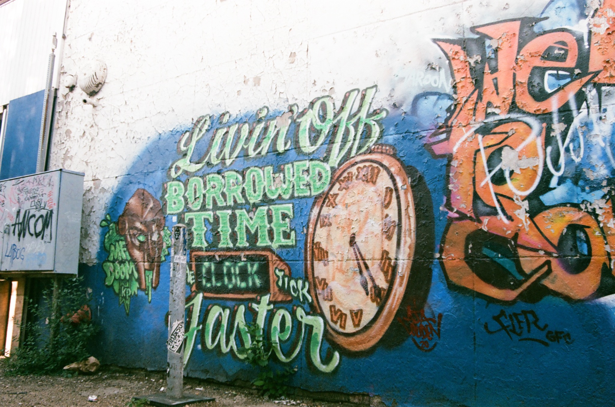graffiti on a peeling wall reads 'livin' off borrowed time' with a clock and green-eyed face.