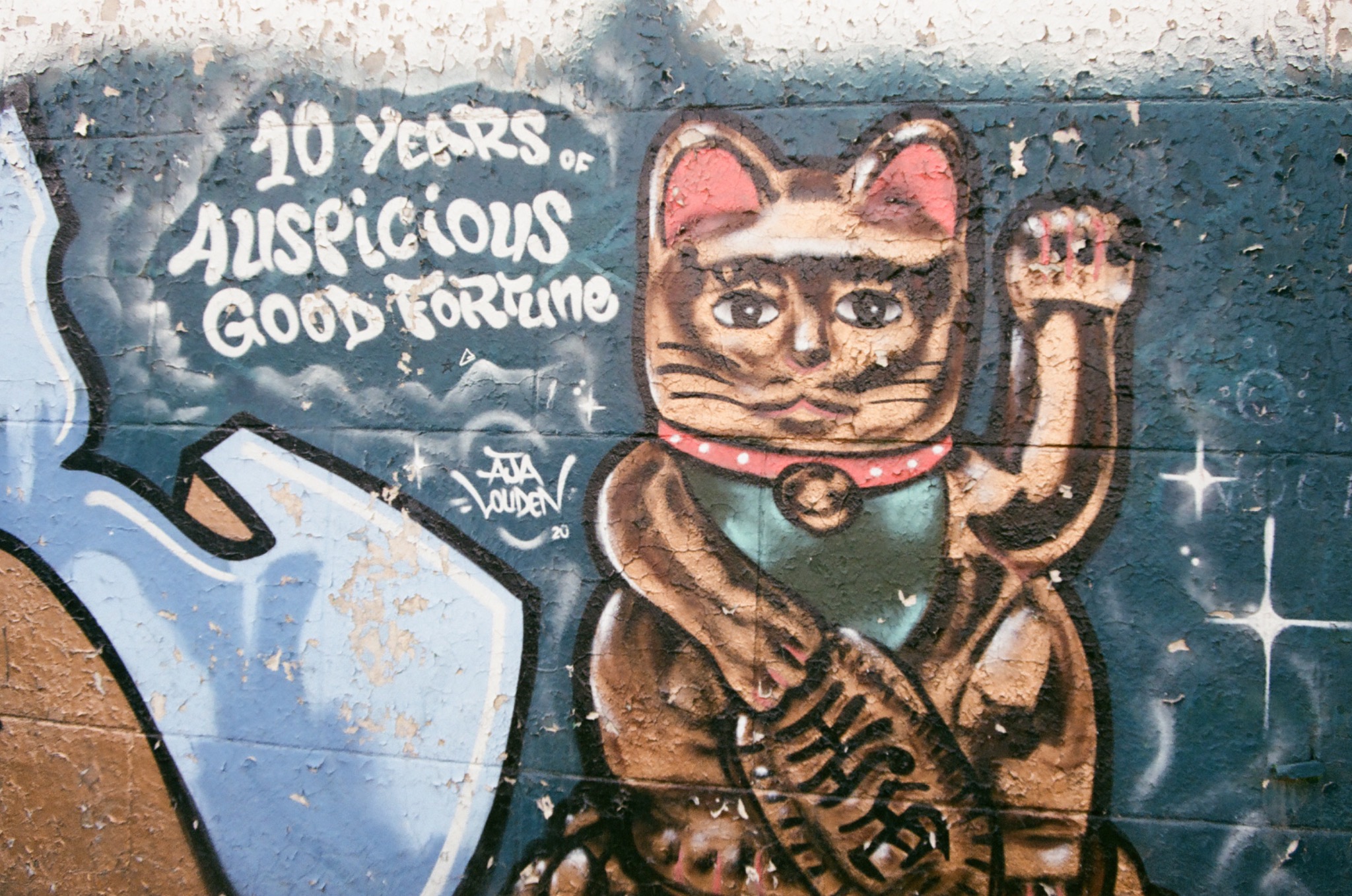 street art of a maneki-neko cat on a textured wall with text "10 years of auspicious good fortune".