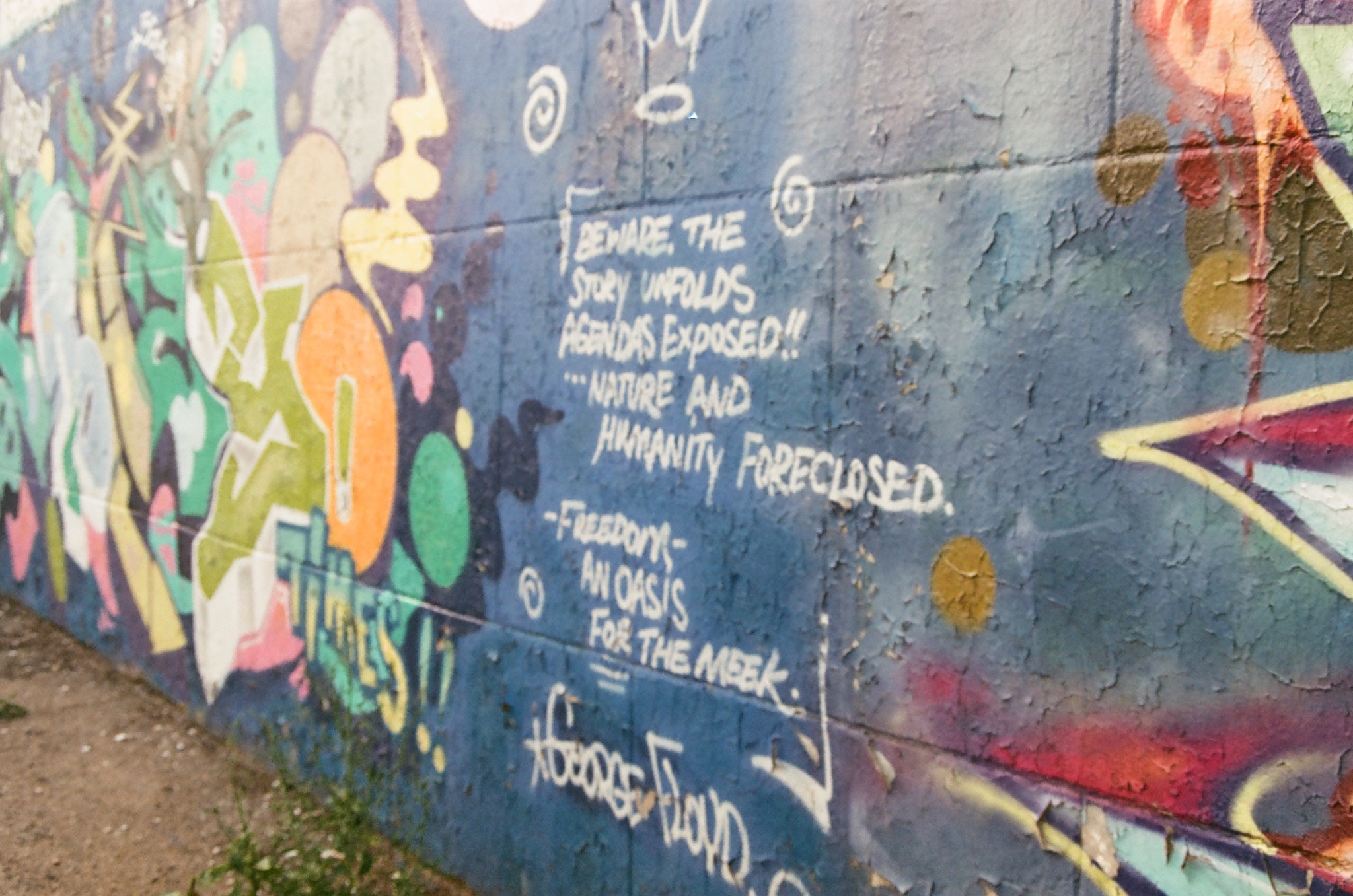 graffiti covered blue wall with peeling paint and white text about freedom and exposed agendas.