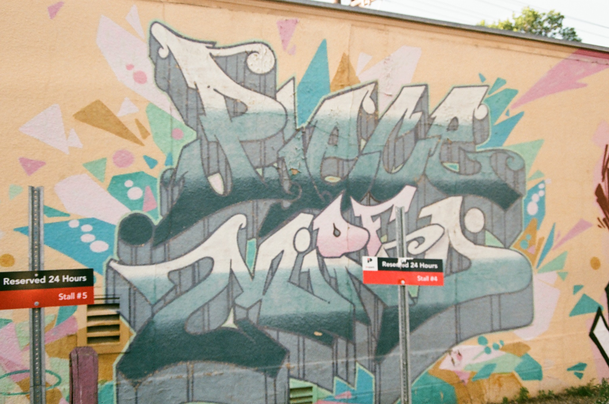 graffiti art on a beige wall with faded teal, white, and pink letters