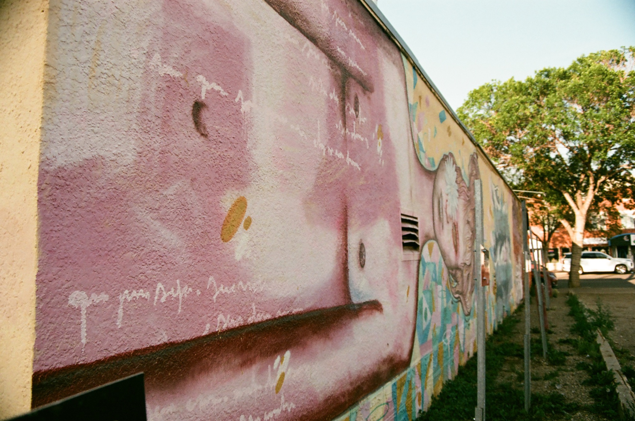 textured pink and white mural on a building wall with faded writing, urban street scene